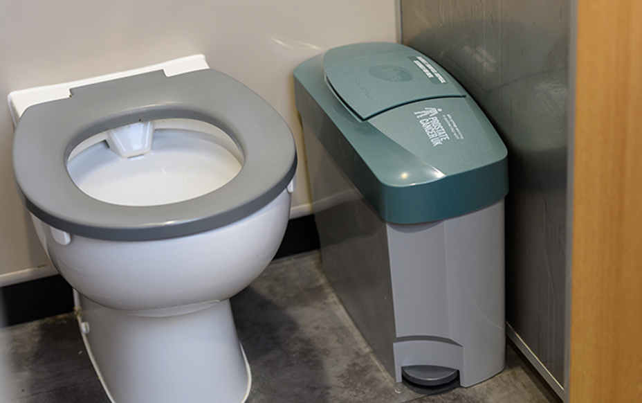 Male incontinance sanitary bin located next to a public toilet in a male washroom