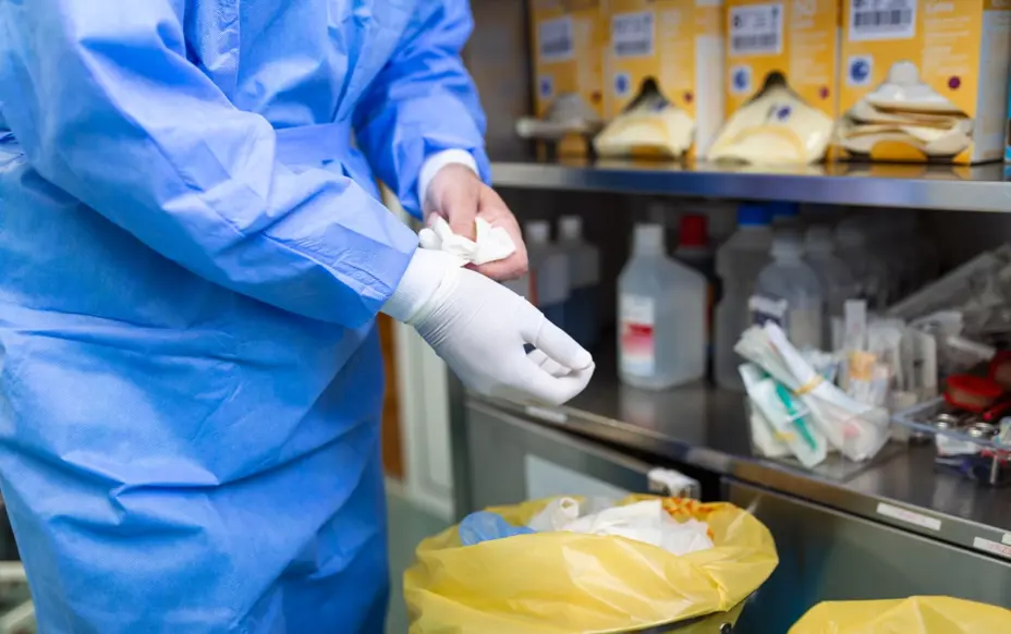 Surgeon removing gloves and putting them into a offensive waste bag