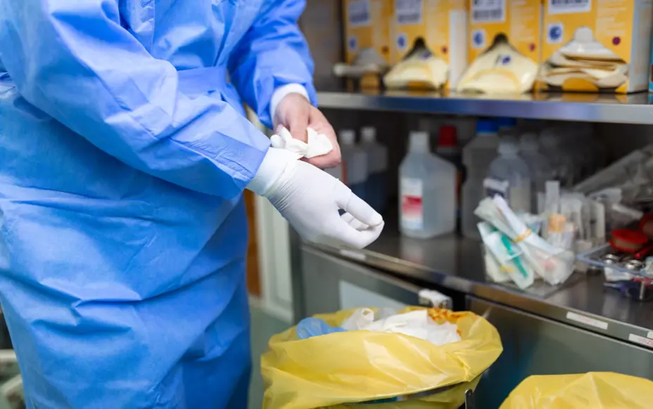 Surgeon removing gloves and putting them into a offensive waste bag